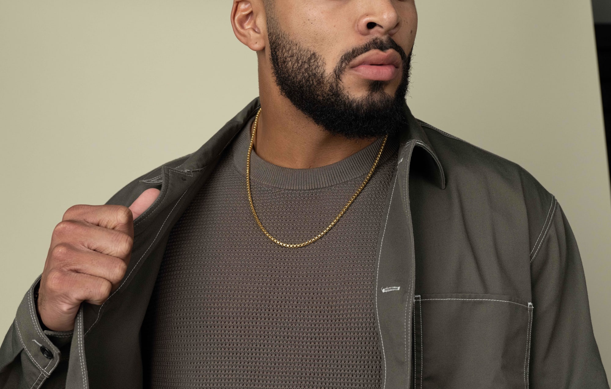 A zoomed-in view of Johnny Middlebrooks wearing the JAXXON gold Round Box Chain, with a grey knit top and a grey shirt jacket.