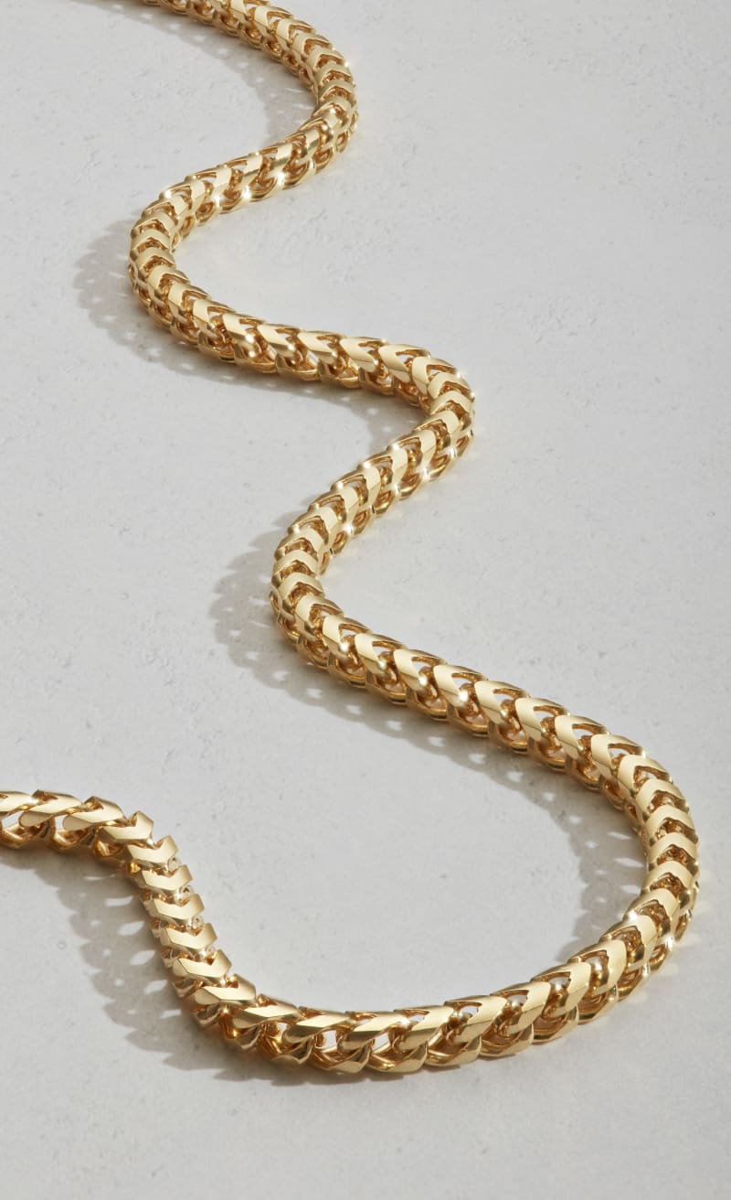 A close-up view of JAXXON's gold 3mm Franco Chain laid out in a wavy pattern on a light grey surface.