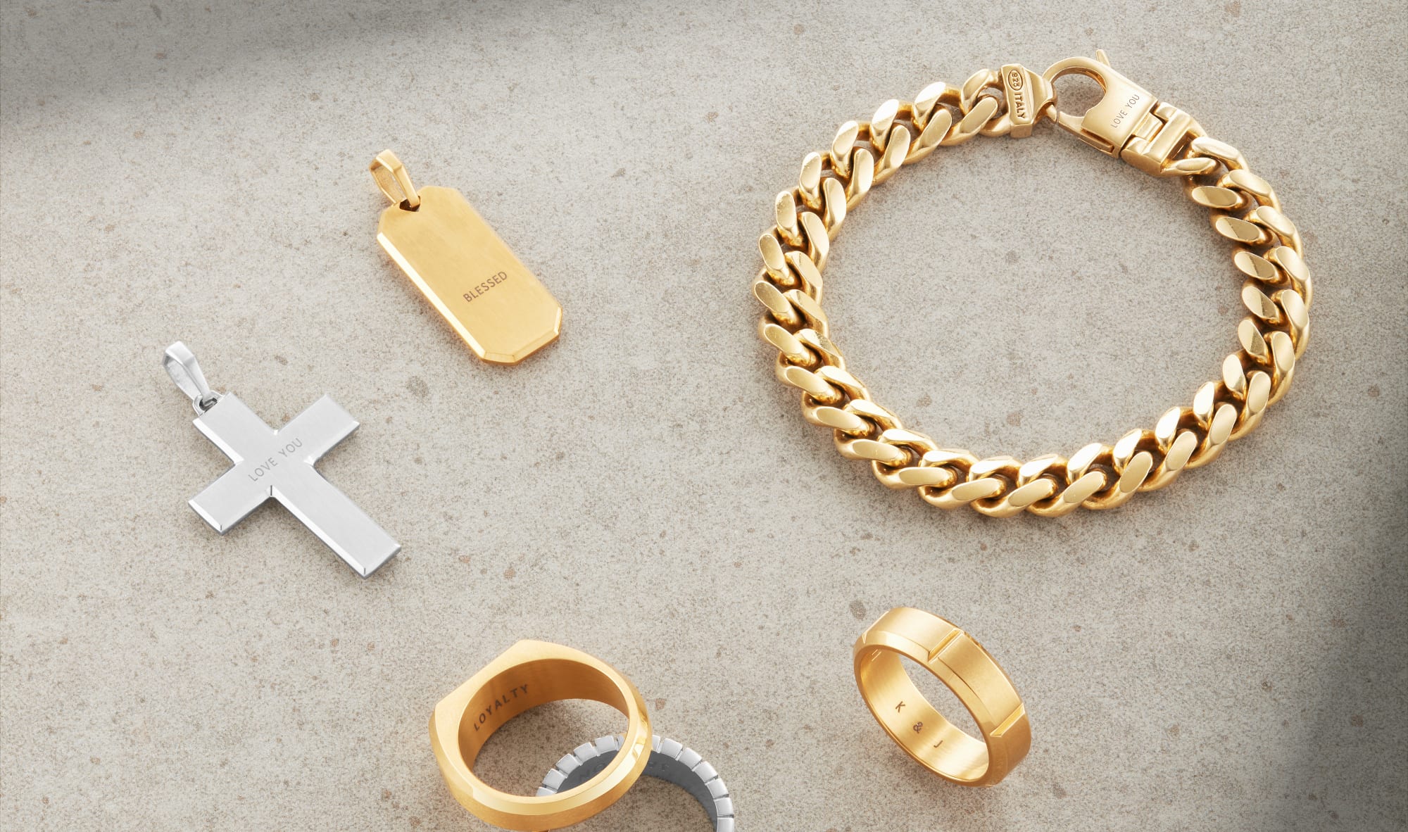 An overhead view of engravable JAXXON jewelry pieces, including the Signet Ring, Mosaic Cross Pendant, and Cuban Link Bracelet.