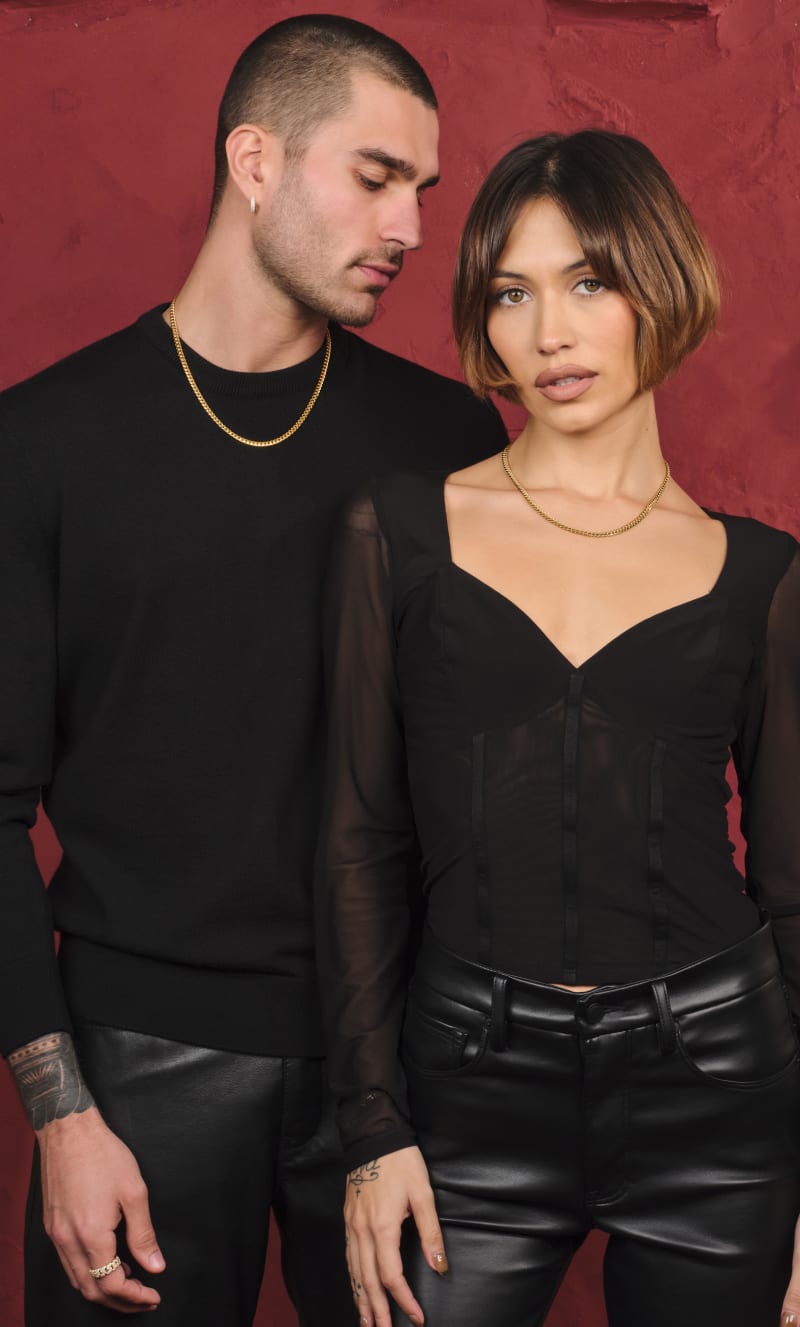 A male and female model standing together wearing the gold JAXXON His and Hers Cuban 5mm Chain Set against a red backdrop.