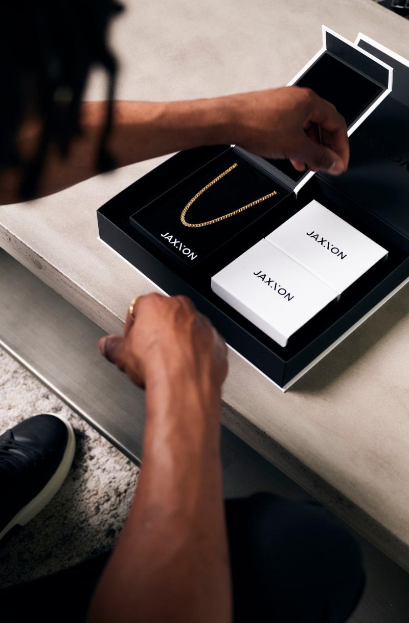 Over-the-shoulder view of a man opening a JAXXON gift box with the gold 5mm Cuban link chain inside.