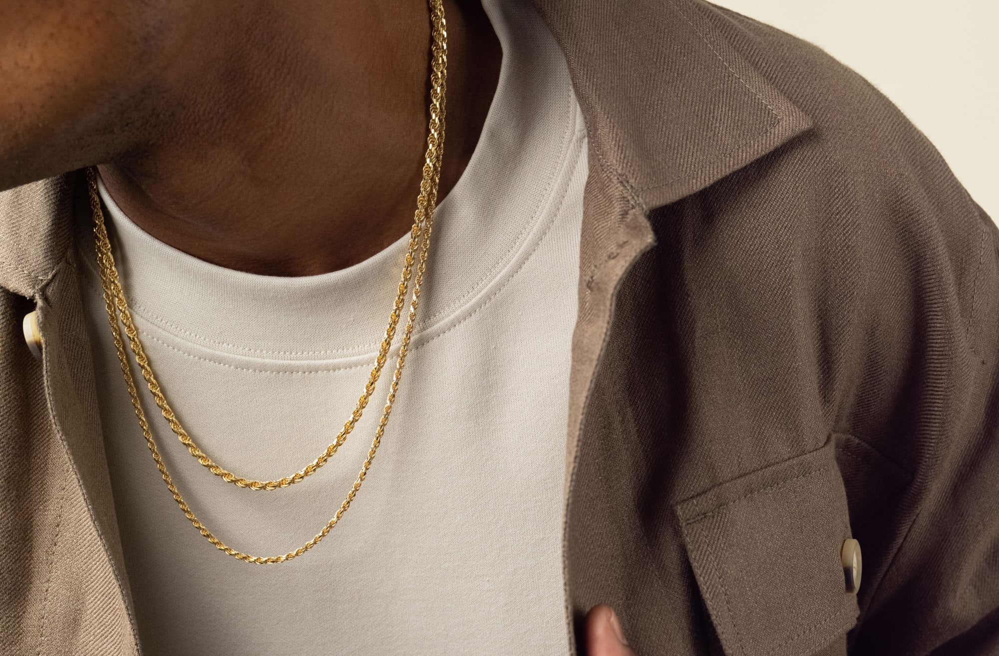 A zoomed-in view of a male model wearing the gold JAXXON Rope Chain Stack styled with a white crew neck tee and grey button down shirt.
