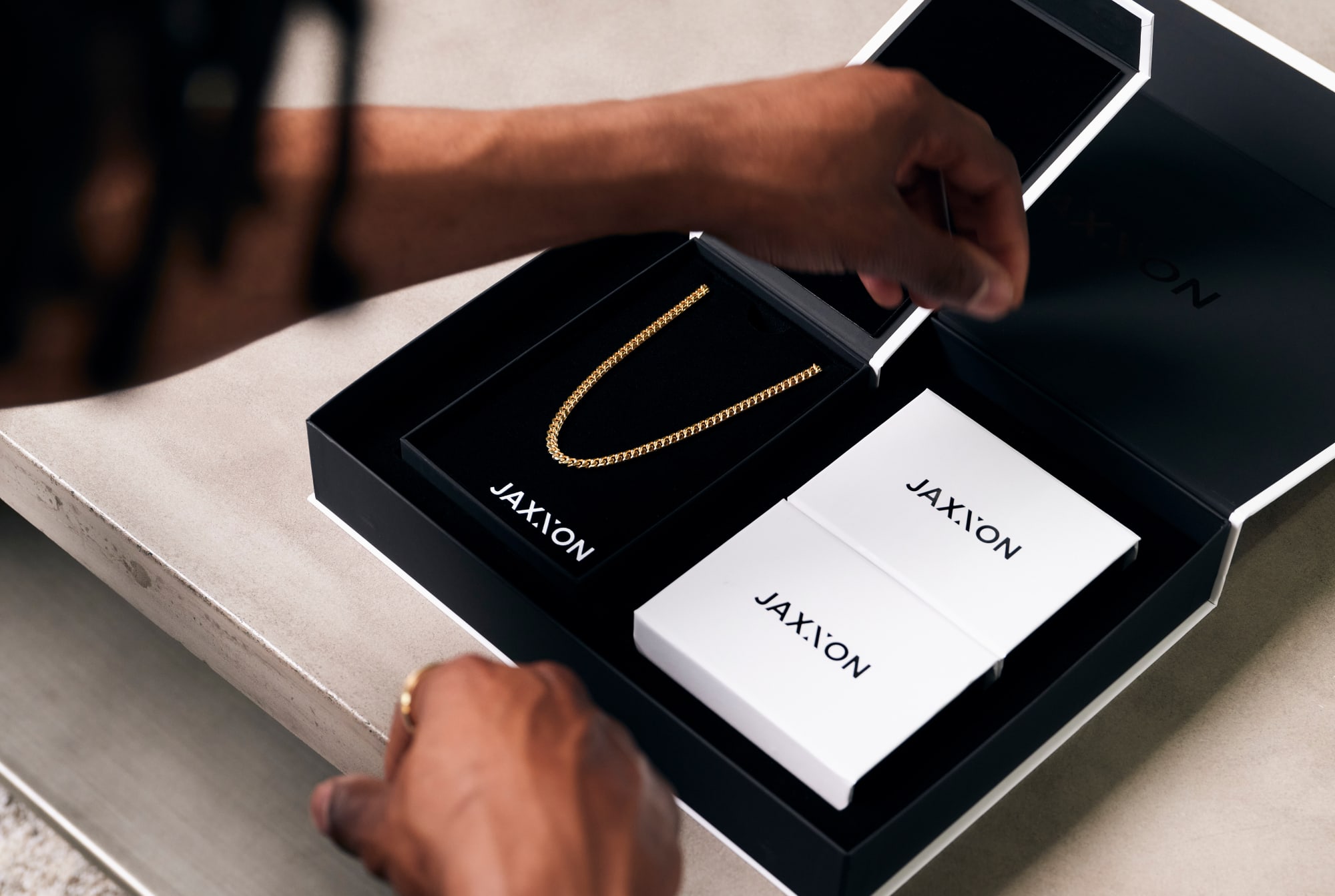 Over-the-shoulder view of a man opening a JAXXON gift box with the gold 5mm Cuban link chain inside.