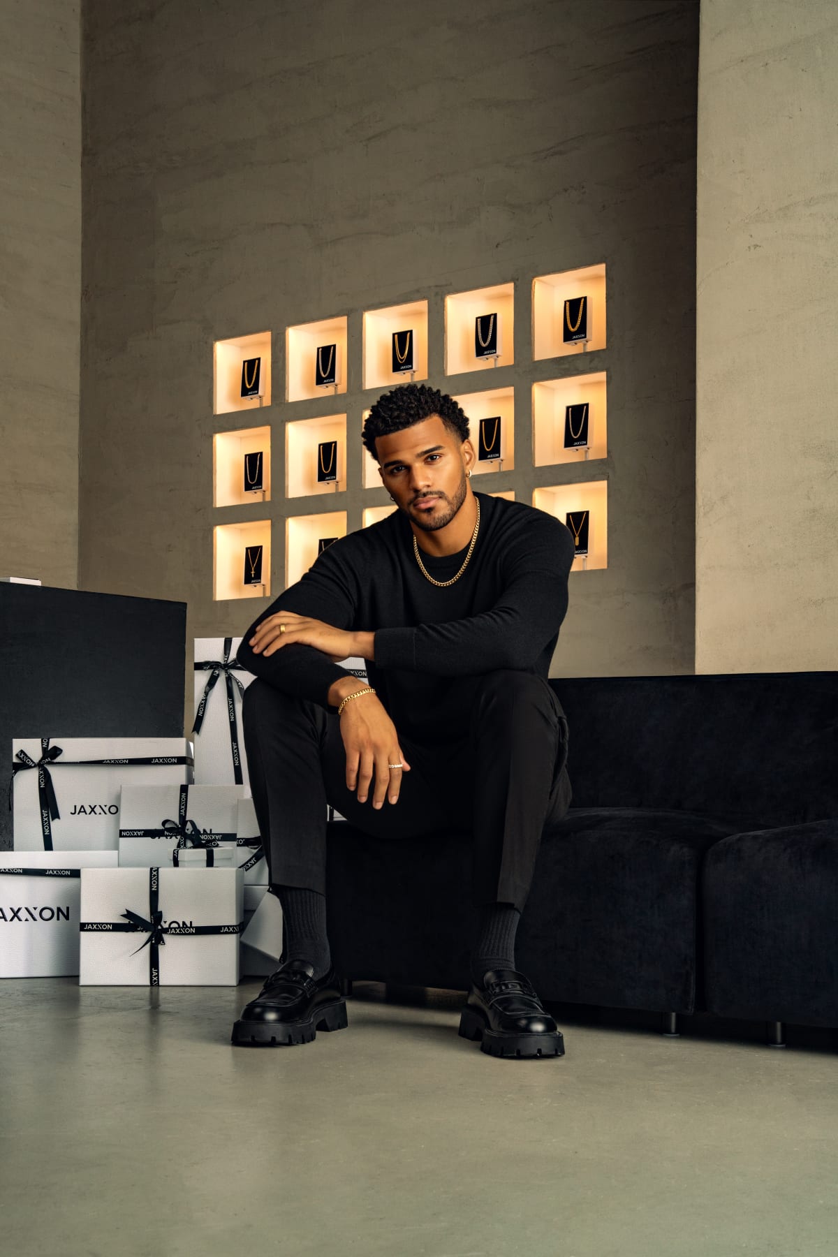 A man seated with JAXXON gift boxes and a wall of JAXXON chains